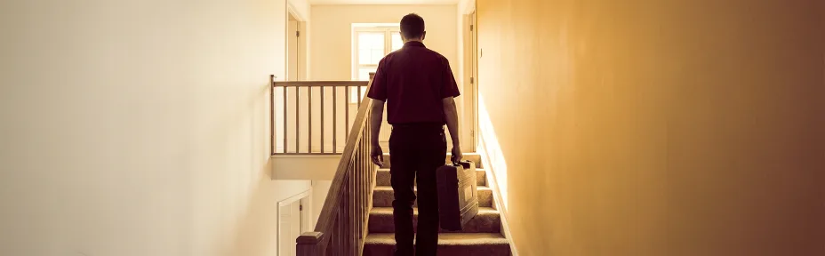 Technician carrying a tool case up the stairs of a two-story home